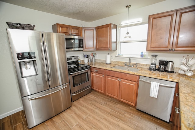 kitchen featuring sink, light hardwood / wood-style flooring, stainless steel appliances, light stone counters, and pendant lighting