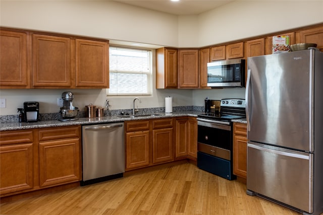 kitchen with light hardwood / wood-style floors, dark stone counters, appliances with stainless steel finishes, and sink