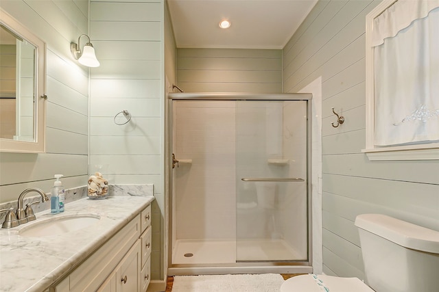 bathroom with an enclosed shower, wooden walls, large vanity, and toilet