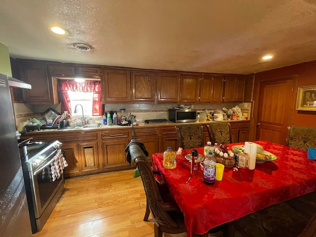 kitchen with backsplash, sink, stainless steel appliances, light hardwood / wood-style flooring, and wall chimney range hood