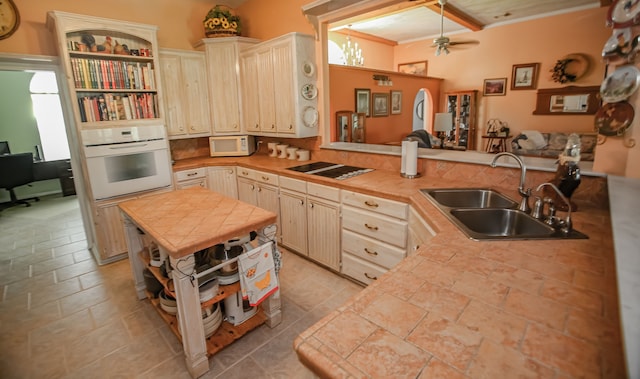 kitchen featuring light tile floors, kitchen peninsula, ceiling fan with notable chandelier, white appliances, and sink