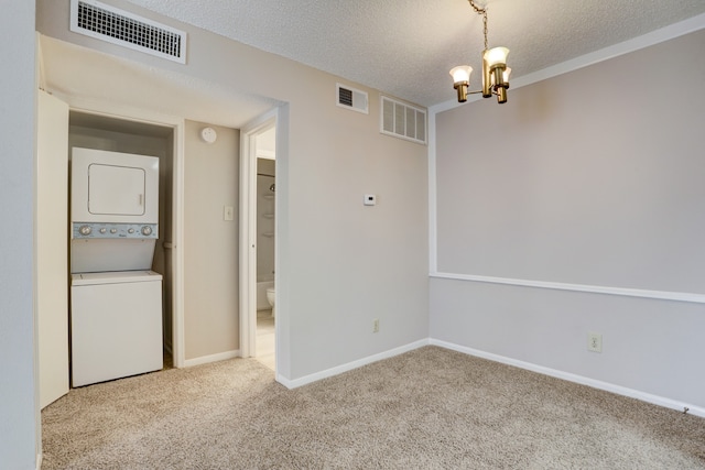 unfurnished room featuring an inviting chandelier, a textured ceiling, stacked washer and dryer, and carpet flooring