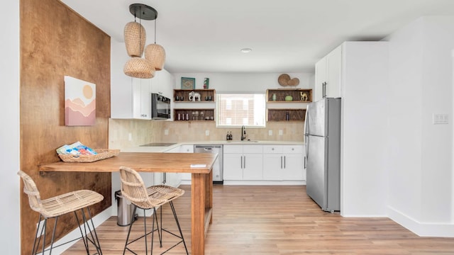 kitchen featuring decorative light fixtures, white cabinetry, appliances with stainless steel finishes, light wood-type flooring, and tasteful backsplash