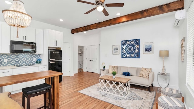 living room featuring beamed ceiling, an AC wall unit, ceiling fan with notable chandelier, and light hardwood / wood-style flooring