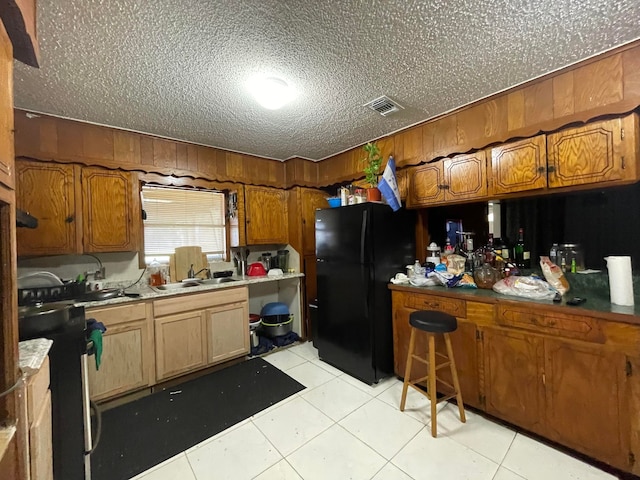 kitchen with black refrigerator, light tile flooring, sink, a textured ceiling, and stove