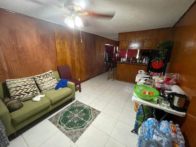 tiled living room featuring ceiling fan, a textured ceiling, and wooden walls