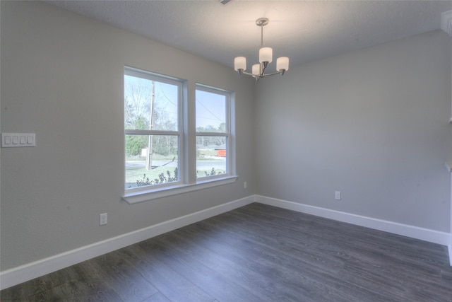 empty room featuring a textured ceiling, dark wood-type flooring, and a chandelier