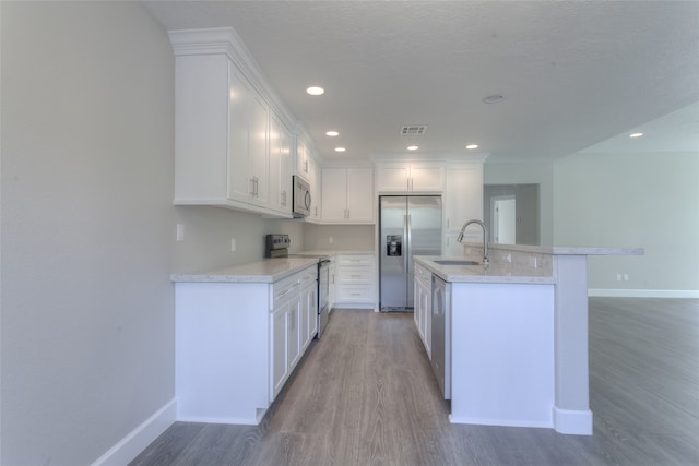 kitchen with white cabinetry, appliances with stainless steel finishes, an island with sink, and hardwood / wood-style floors