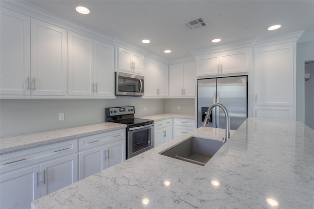 kitchen with appliances with stainless steel finishes, sink, light stone counters, and white cabinetry