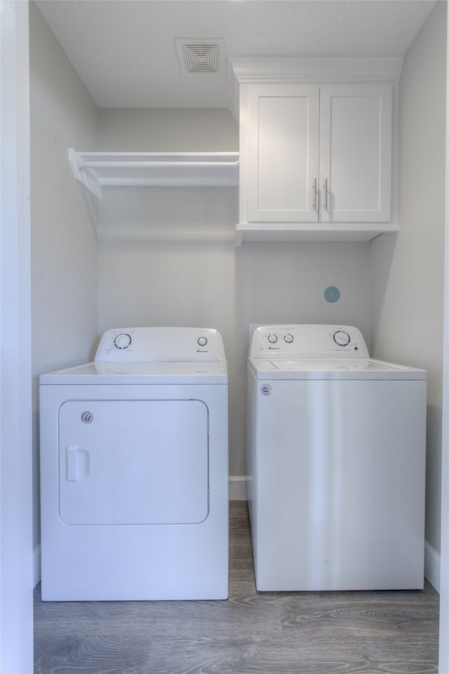 clothes washing area with cabinets, washing machine and dryer, and hardwood / wood-style flooring