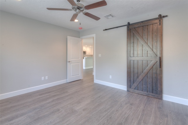 unfurnished bedroom featuring a barn door, ceiling fan, and light wood-type flooring