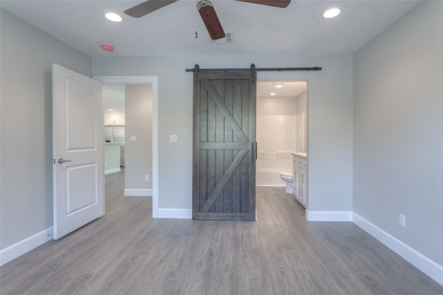 unfurnished bedroom featuring a barn door, ceiling fan, light hardwood / wood-style flooring, and ensuite bathroom