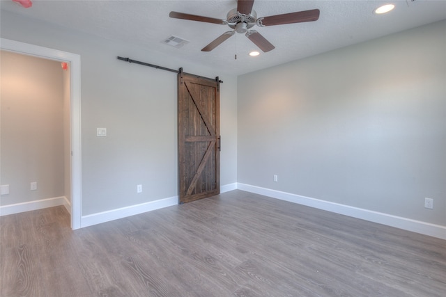 unfurnished bedroom featuring ceiling fan, hardwood / wood-style floors, a barn door, and a textured ceiling