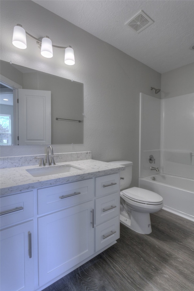 full bathroom featuring wood-type flooring, a textured ceiling, toilet, vanity, and shower / bathtub combination