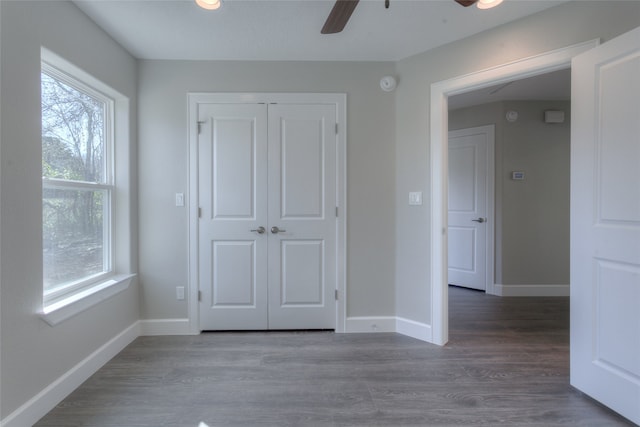 unfurnished bedroom featuring multiple windows, dark wood-type flooring, ceiling fan, and a closet