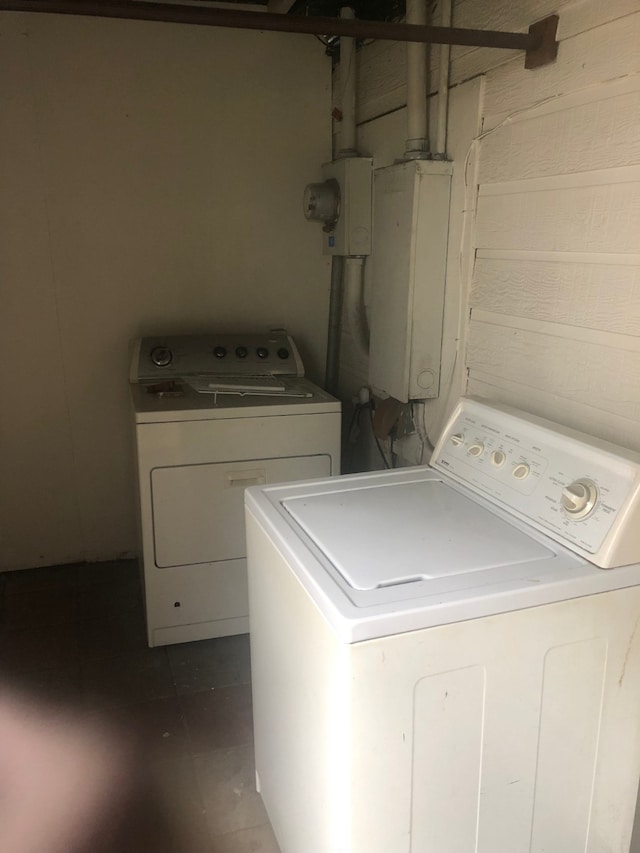 laundry room featuring wood walls, dark tile flooring, and washing machine and dryer