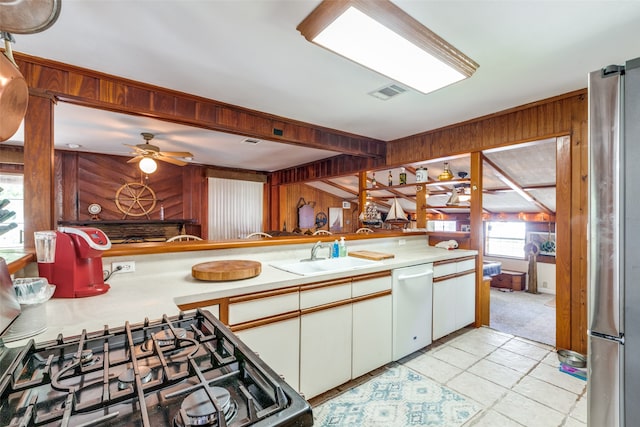 kitchen with ceiling fan, wooden walls, white dishwasher, light tile patterned floors, and sink