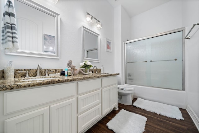 full bathroom with toilet, wood-type flooring, dual bowl vanity, and shower / bath combination with glass door