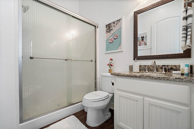 bathroom featuring toilet, vanity, hardwood / wood-style flooring, and a shower with shower door