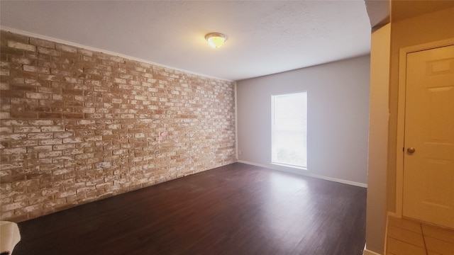 spare room with brick wall, dark hardwood / wood-style flooring, and ornamental molding