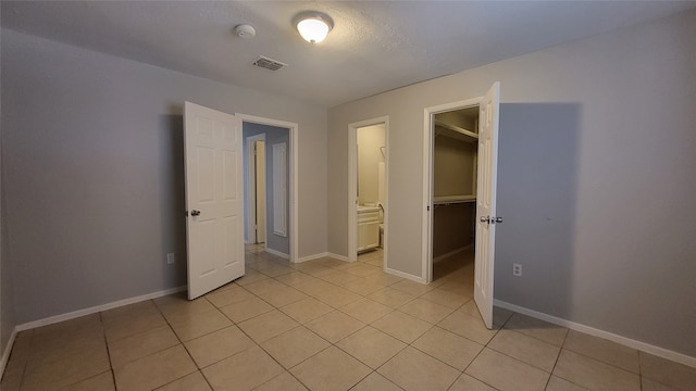 unfurnished bedroom with a walk in closet, a closet, ensuite bathroom, and light tile floors