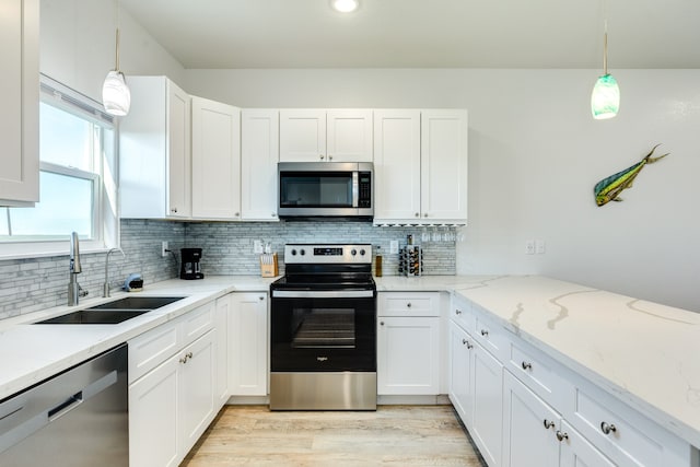 kitchen with appliances with stainless steel finishes, decorative light fixtures, light hardwood / wood-style floors, and light stone counters