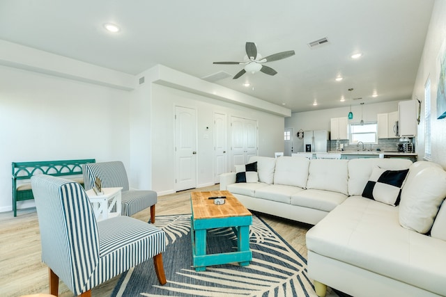 living room featuring ceiling fan, sink, and light wood-type flooring