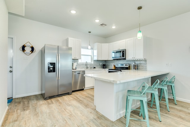 kitchen featuring appliances with stainless steel finishes, hanging light fixtures, white cabinetry, and light hardwood / wood-style floors