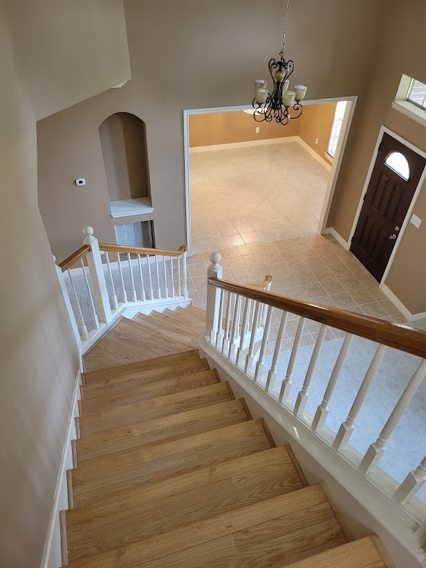 stairway with a chandelier, light wood-type flooring, and a high ceiling