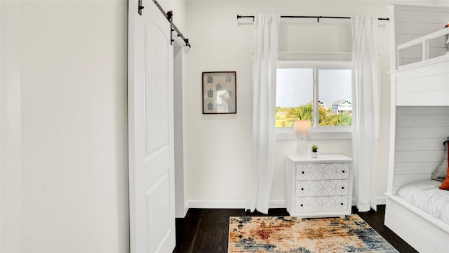 bedroom with a barn door and dark hardwood / wood-style floors