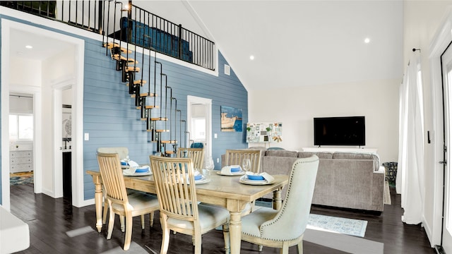 dining space featuring dark hardwood / wood-style flooring, wooden walls, and high vaulted ceiling