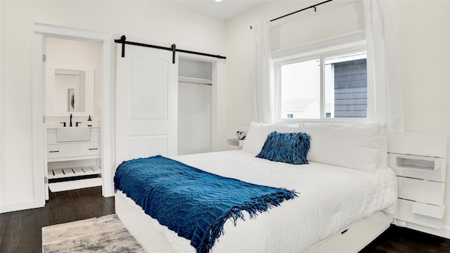 bedroom featuring dark hardwood / wood-style flooring, a barn door, ensuite bath, a closet, and sink