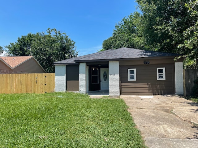 view of front of property with a front yard, fence, concrete driveway, brick siding, and roof with shingles