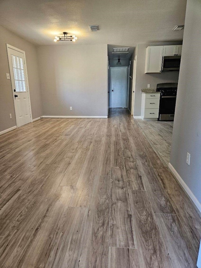 unfurnished living room with visible vents, baseboards, a textured ceiling, and wood finished floors