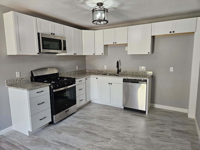kitchen with white cabinets, baseboards, a sink, stainless steel appliances, and light stone counters