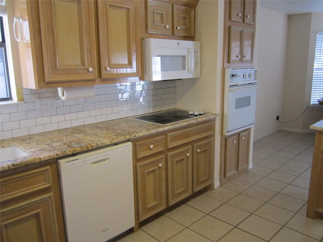 kitchen featuring light tile patterned flooring, white appliances, light stone counters, and backsplash