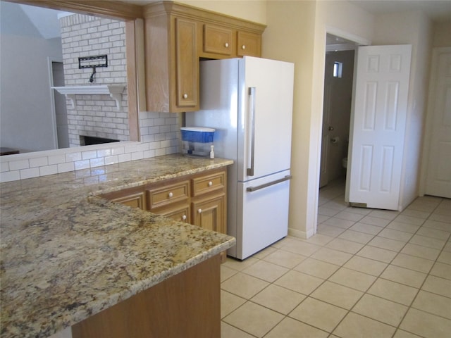 kitchen featuring white refrigerator, light tile patterned flooring, light stone countertops, and backsplash