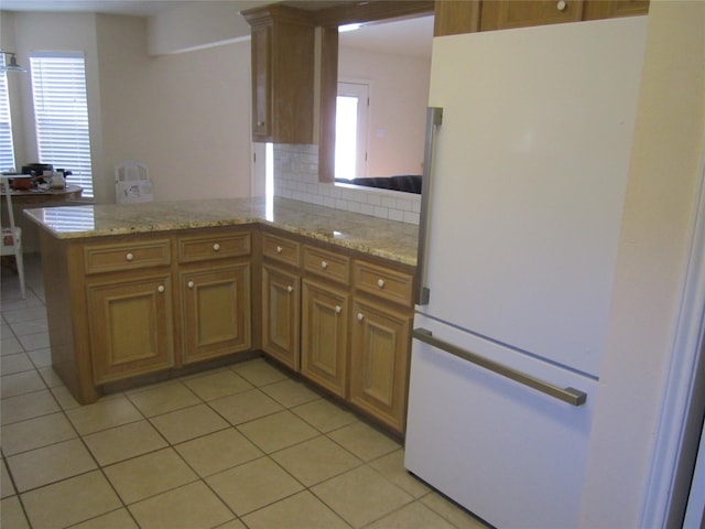 kitchen featuring white refrigerator, tasteful backsplash, light tile patterned flooring, light stone counters, and kitchen peninsula