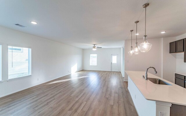 interior space featuring decorative light fixtures, light hardwood / wood-style floors, ceiling fan, dark brown cabinets, and sink