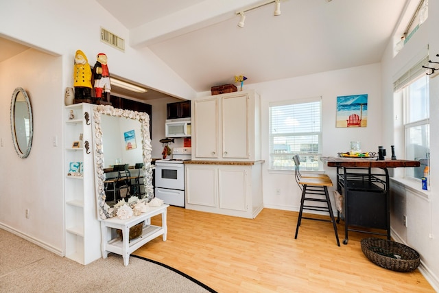 kitchen featuring white appliances, lofted ceiling with beams, a healthy amount of sunlight, and white cabinetry