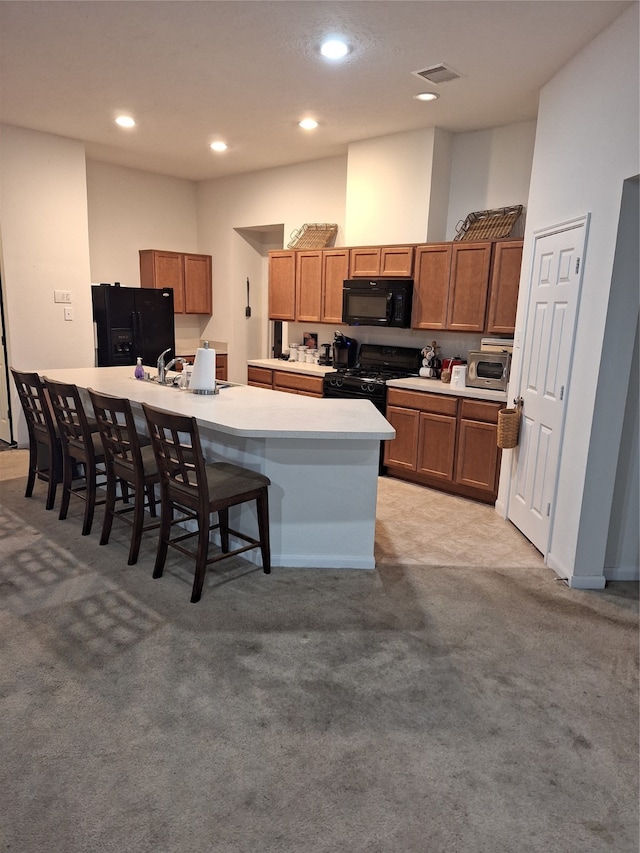 kitchen with a kitchen bar, light carpet, black appliances, and an island with sink