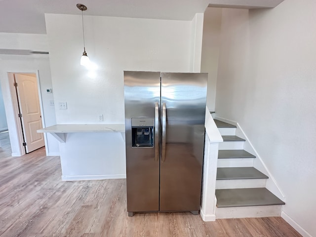 kitchen featuring light hardwood / wood-style floors, light stone countertops, white cabinetry, stainless steel refrigerator with ice dispenser, and pendant lighting