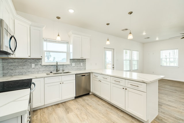 kitchen with light hardwood / wood-style floors, appliances with stainless steel finishes, kitchen peninsula, pendant lighting, and tasteful backsplash