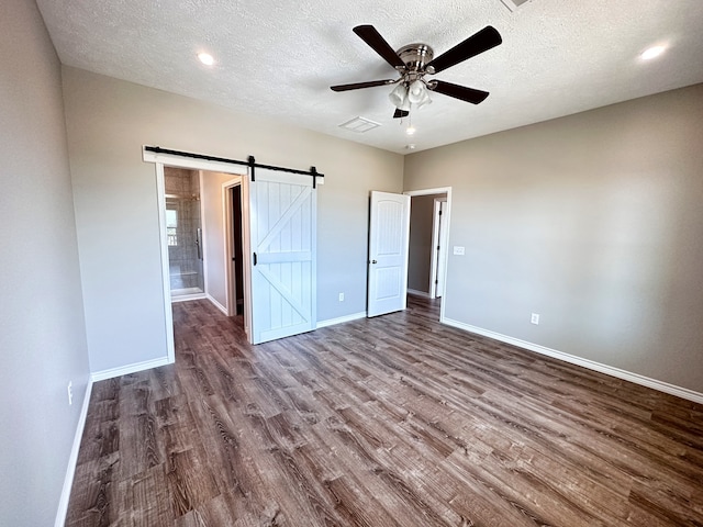 unfurnished bedroom featuring a barn door, ceiling fan, a textured ceiling, and dark hardwood / wood-style flooring