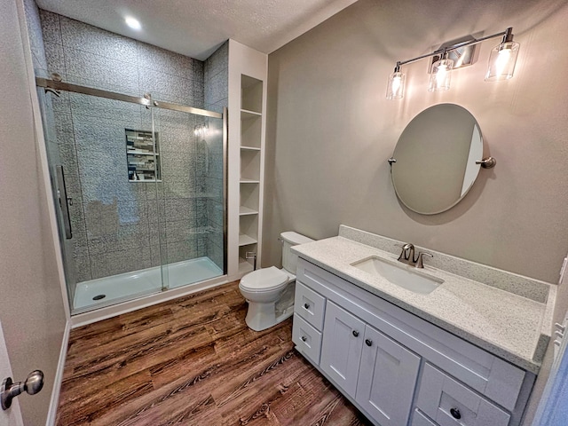 bathroom with toilet, oversized vanity, a textured ceiling, wood-type flooring, and an enclosed shower