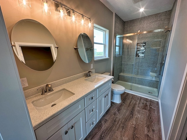 bathroom with toilet, double sink, vanity with extensive cabinet space, hardwood / wood-style floors, and a shower with door