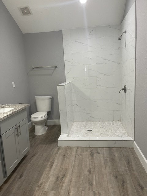 bathroom featuring a tile shower, hardwood / wood-style flooring, vanity, and toilet