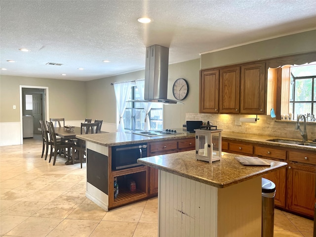 kitchen with range hood, sink, dark stone counters, a kitchen island, and tasteful backsplash