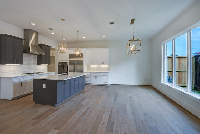 kitchen with decorative light fixtures, wall chimney range hood, appliances with stainless steel finishes, and tasteful backsplash