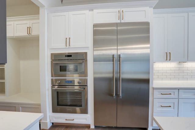 kitchen with appliances with stainless steel finishes, white cabinetry, tasteful backsplash, and dark wood-type flooring